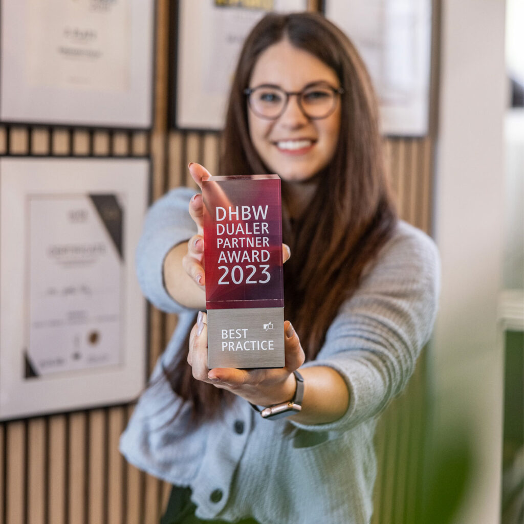Eine Mitarbeiterin hält den DHBW Dualen Partner Award 2023 in die Kamera.