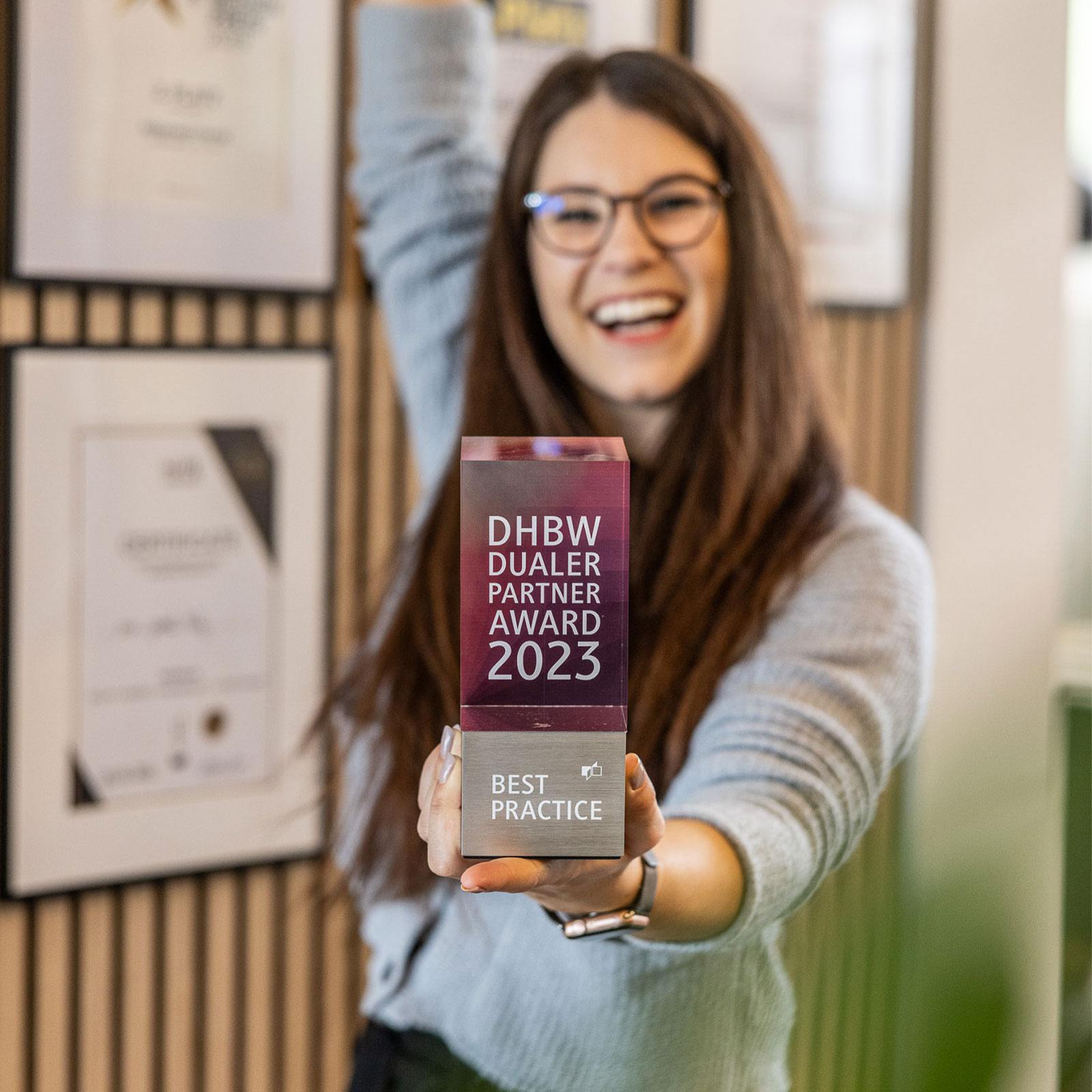 Eine Mitarbeiterin hält den DHBW Dualen Partner Award 2023 in die Kamera und feiert.