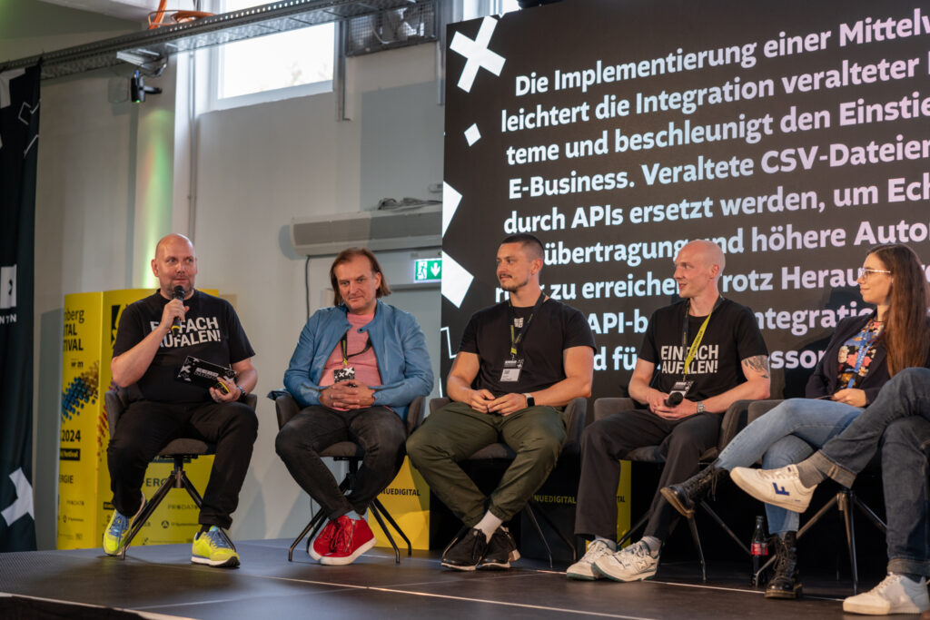 Sechs Personen sitzen in Stühlen auf einer Bühne und diskutieren.