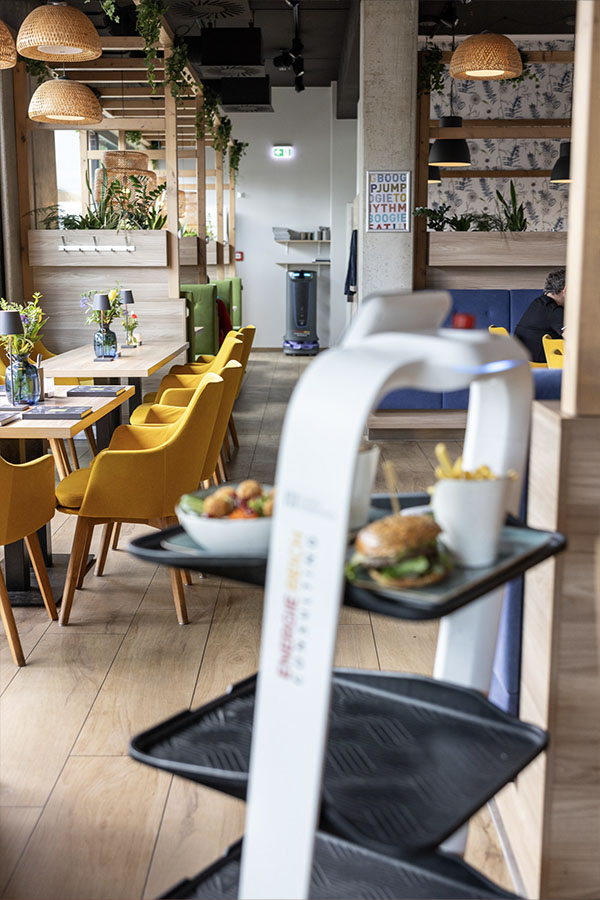 Das moderne Restaurant von Eatery. Im Vodergrund fährt ein Servierroboter mit Essen.