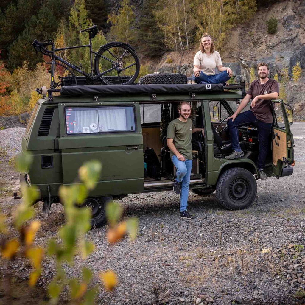 Drei Personen posieren vor einem Camping-Van.