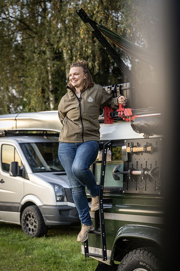 Eine junge Frau steigt die Leiter ihres Jeeps herab.