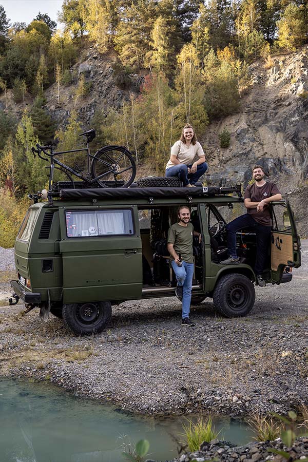 Drei junge Menschen posieren vor einem Camping-Van.