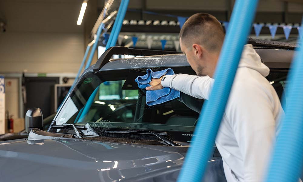 Ein junger Mann putzt die Frontscheibe seines Autos.